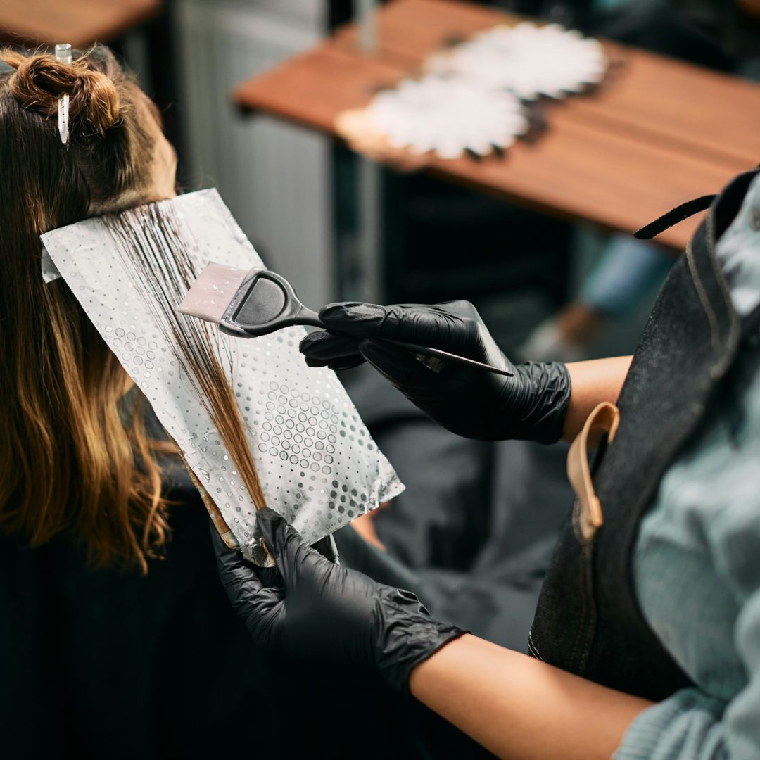 Close-up of hairdresser dyeing customer's hair at the salon.